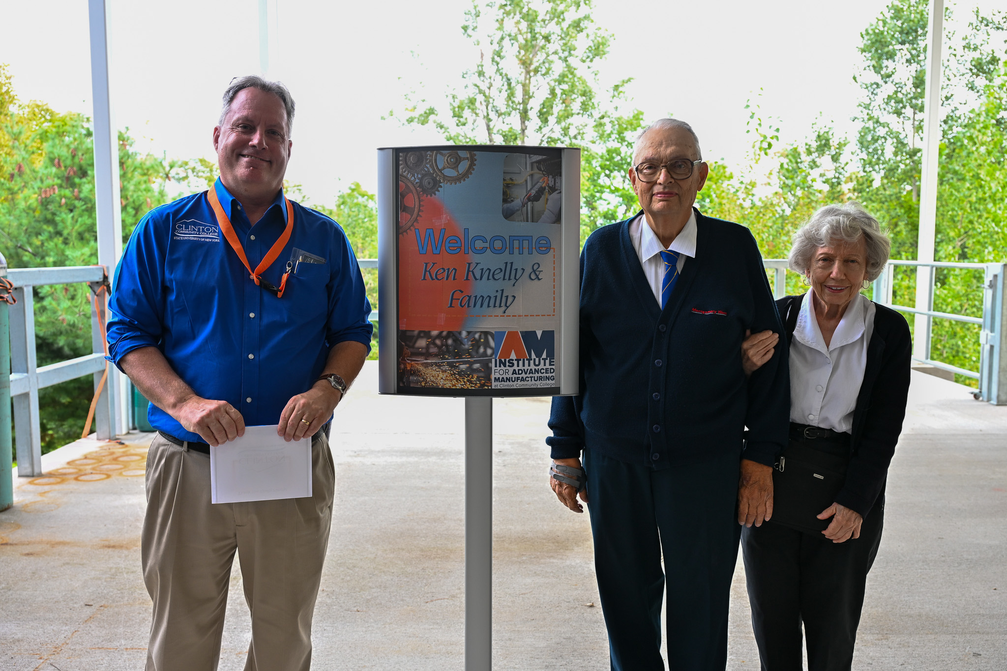 Three people standing next to a sign that says 'Welcome Ken Knelly and family. Institute for Advanced Manufacturing' while out on a loading dock