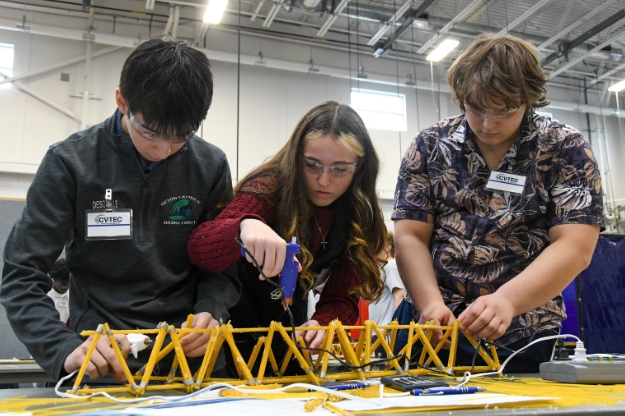 Three students working on a bridge made of spaghetti