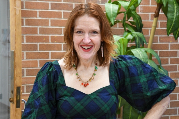 A person standing in front of a brick wall and green plant